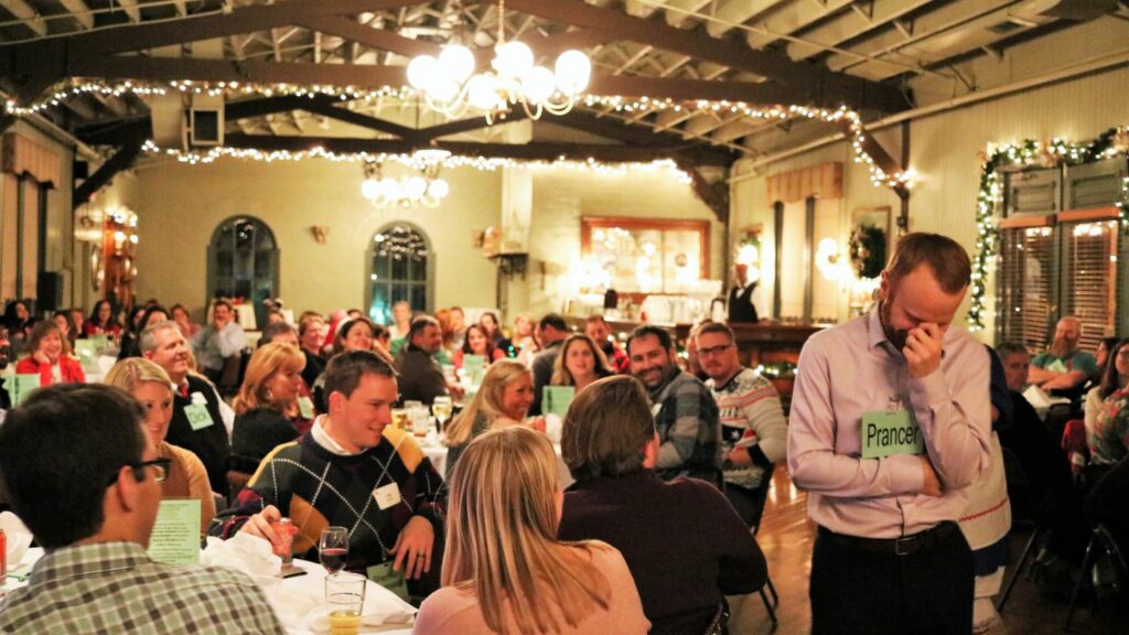 Audience at company holiday party laughing while coworker play part in murder mystery