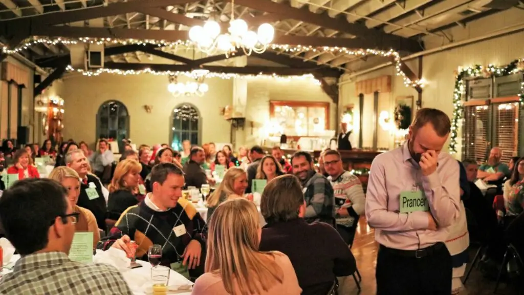 Audience at company holiday party laughing while coworker play part in murder mystery